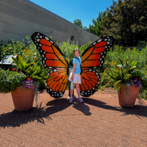 A girl smiling in front of a butterfly sculpture